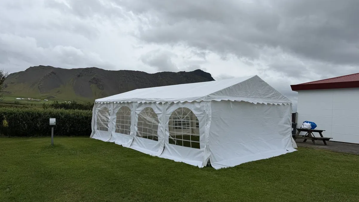 White 5×8 m RentEvent party tent set up on a lawn below a mountain